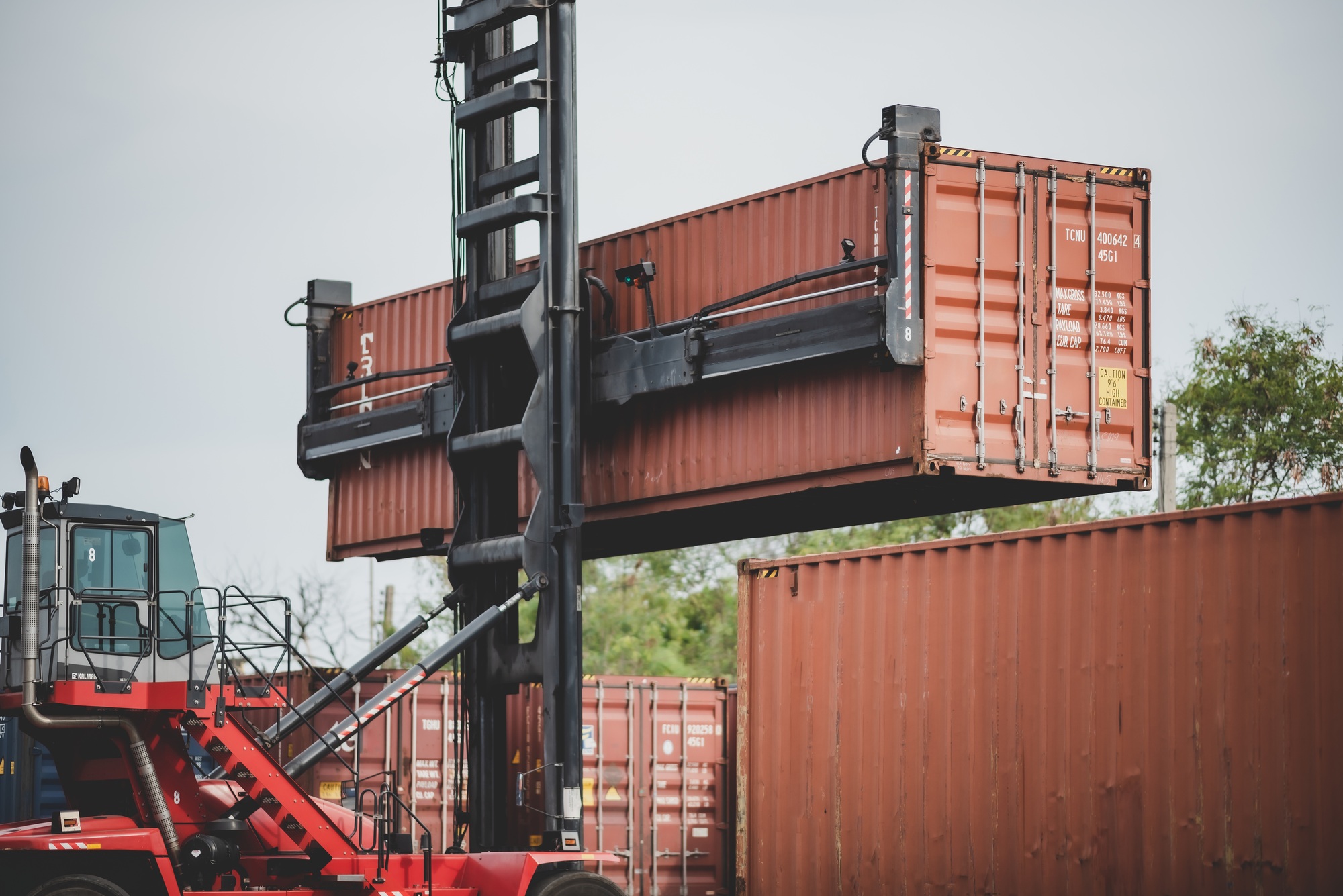 Forklift truck lifting cargo container in shipping yard or dock yard with cargo container stack